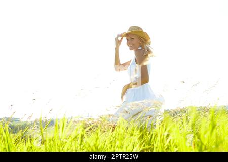 Ill always be a country girl. A beautiful young blonde woman standing in a meadow wearing a sunhat on a warm summers day Stock Photo