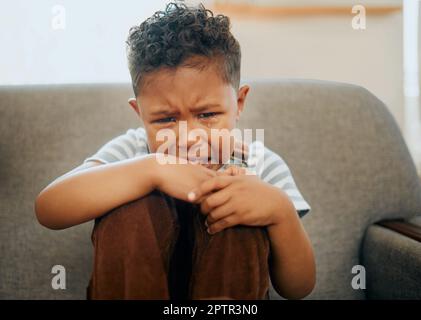 One mixed race little boy crying on the sofa at home. African American child suffering from PTSD after being abused and neglected. Grieving little bla Stock Photo