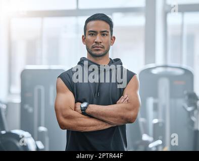 Portrait of one serious asian trainer alone in gym. Handsome focused coach standing with arms crossed after workout in health club. Young confident ma Stock Photo