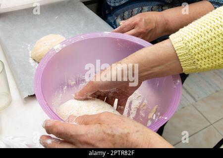 The process of kneading Portuguese sweet bread dough. Close-up of two women hands in the kitchen moulding dough in a plastic bowl Stock Photo