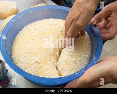 The process of kneading Portuguese sweet bread dough. Close-up of women hands separating dough in a plastic bowl to be moulded on the kitchen counter Stock Photo