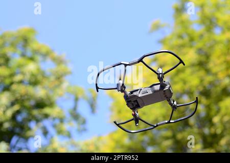 Drone with photocamera take off from land and flying for take aerial photo at sunset evening front of trees Stock Photo