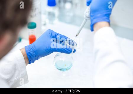 Female researcher with dropper dripping liquid into a test tube in ...