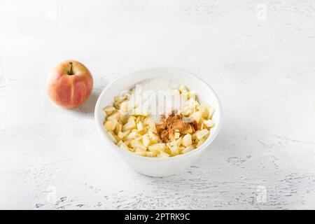 White ceramic bowl with sliced apples with sugar and cinnamon for apple pie filling on a light gray background Stock Photo