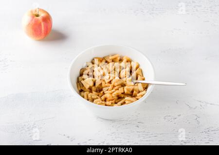 White ceramic bowl with sliced apples with sugar and cinnamon for apple pie filling on a light gray background Stock Photo