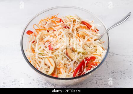 Glass bowl with shredded cabbage with grated carrots, apples and sweet peppers on a light gray background. Cooking delicious homemade food Stock Photo