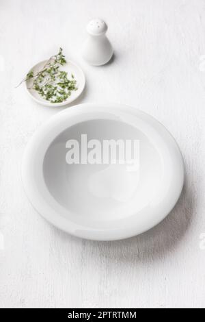 White empty plate, salt shaker, plate with greens on a light gray background, top view Stock Photo