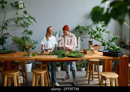 Two happy and smiling florists working together at creative workshop studio. Young man and woman making beautiful home decoration for design interior Stock Photo