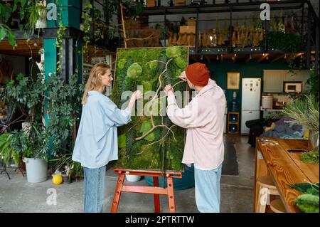 Two young hipster designers working on floral collage for home design interior at florist shop Stock Photo