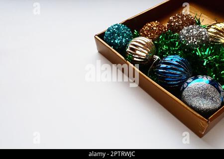 trendy Christmas decorations, colorful balls and tinsel in the lid of a gift box. Shiny beige or brown box for gifts or storage. New Year's Christmas Stock Photo