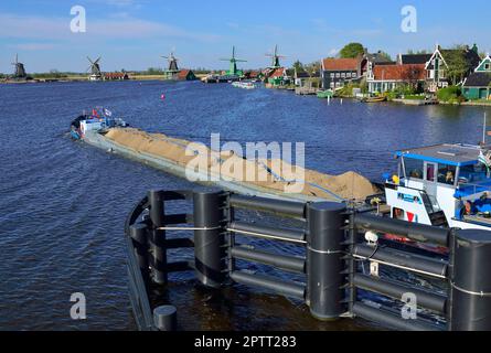 Canal boat transporting ballast on the Zaan River  with The Zaanse Schans windmills in the distance  housing  seven museums and working windmills Stock Photo