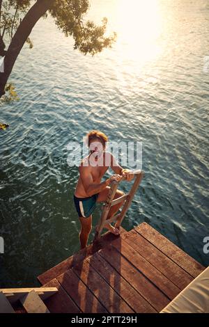 The young man goes down the ladder to swim in the river on a beautiful summer day. Summer, river, vacation Stock Photo