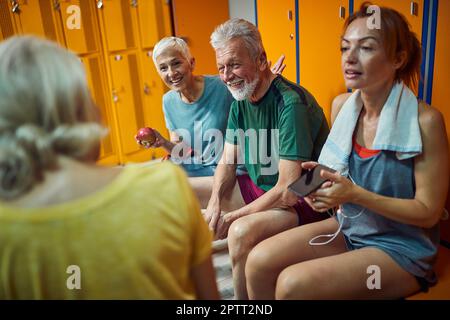 Senior couple with friends sitting in dressing room after workout talking and relxing. Health, wellness, senior life concept. Stock Photo