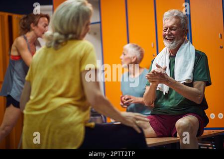 Group of four people in gym locker room, senior man and woman having a joyful conversation sitting facing each other. Health, senior life, wellness co Stock Photo