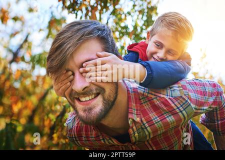Cropped shot of an adorable young boy closing his fathers eyes while being piggybacked outside during autumn. Stock Photo