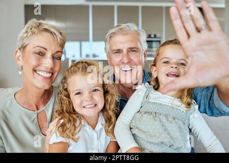 A happy caucasian mature couple bonding with their adopted kids in the living room. Two sisters relaxing with their grandparents while taking selfies Stock Photo