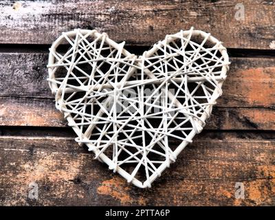 A heart woven from rustic light rods or threads. Wicker form handmade. Valentine's Day. Postcard. Wooden texture background. Love concept. Stock Photo