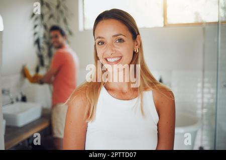 Young caucasian couple sharing a bathroom with focus on happy young woman smiling while looking at the camera in the foreground while waiting to get r Stock Photo