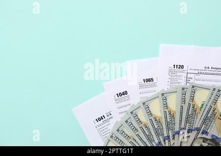 Tax forms lies near hundred dollar bills and blue pen on a light blue background. Income tax return. Stock Photo