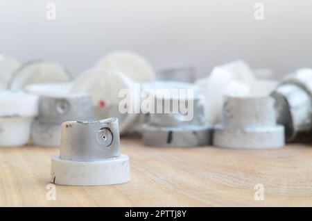 Several plastic nozzles from a paint sprayer that lie on a wooden surface against a gray wall background. The caps are smeared in chrome paint. The co Stock Photo