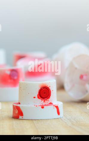 Several plastic nozzles from a paint sprayer that lie on a wooden surface against a gray wall background. The caps are smeared in red paint. The conce Stock Photo