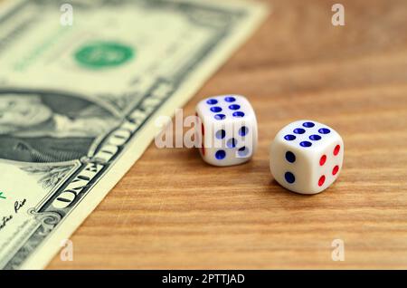 White dice are next to a dollar bill of US dollars on a wooden background. The concept of gambling with rates in monetary units Stock Photo