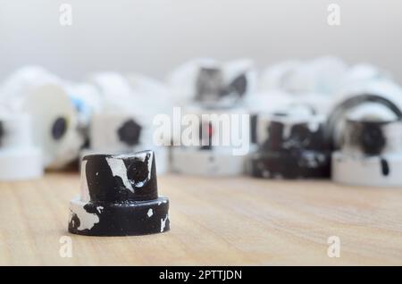 Several plastic nozzles from a paint sprayer that lie on a wooden surface against a gray wall background. The caps are smeared in black paint. The con Stock Photo