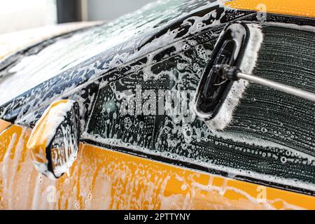 Yellow car side window washed in self service carwash. rush leaves strokes in shampoo and foam on glass. Stock Photo