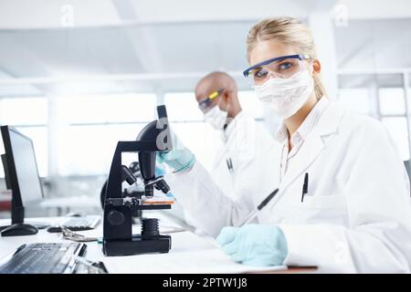Somewhere, something incredible is waiting to be discovered. Portrait of a gorgeous female scientist in front of a microscope with a male colleague in Stock Photo