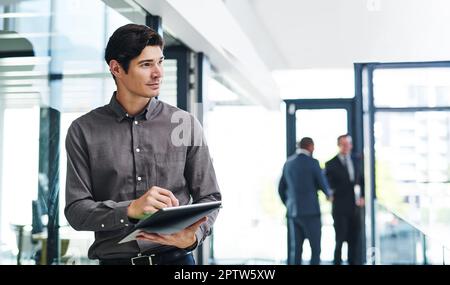 Hes got visions to bring to life. a handsome young businessman looking thoughtful while holding a digital tablet in a modern office. Stock Photo