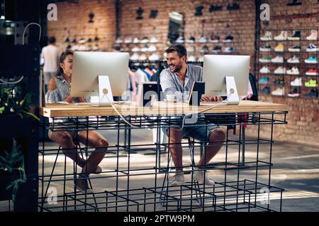 Young man and woman in store working on their pc, and laughing. Teamwork, colleagues, customer service concept. Stock Photo