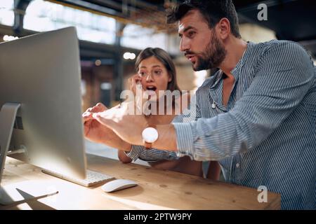 Young man and woman having a business meeting, creative designers talking in front of desktop computer looking at screen. Close up photo. Stock Photo