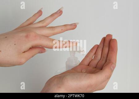 Close-up of woman using hand sanitizer, white background, long nails Stock Photo