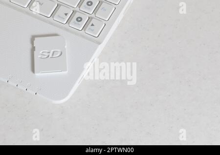 A compact SD memory card lies on a white netbook. The digital information storage device is ready for use. Concept of modern technologies Stock Photo