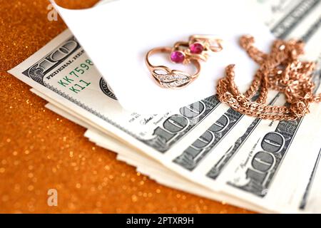 Expensive golden jewerly ring, earrings and necklace with big amount of US dollar bills on luxury glitter golden background surface. Pawnshop or jewer Stock Photo