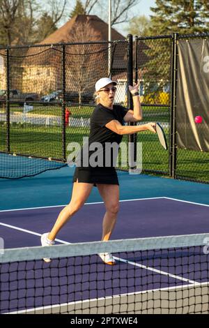 A female pickleball player returns a bright pink ball on a dedicated