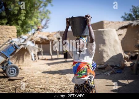 An African woman carries a bucket of water on her head and her baby on her back in Segou Region, Mali, West Africa. 2022 Mali drought and hunger crisis. Stock Photo