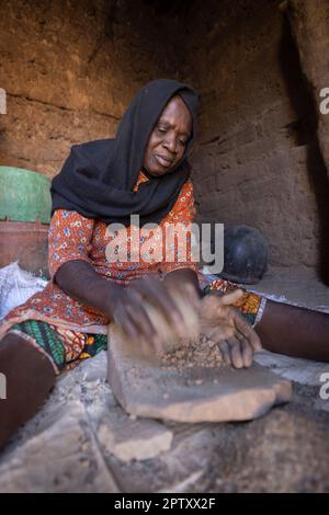 An elderly woman crushes rocks and minerals for making the patina of cooking pots for a meager livelihood in Segou Region, Mali, West Africa. 2022 Mali drought and hunger crisis. Stock Photo