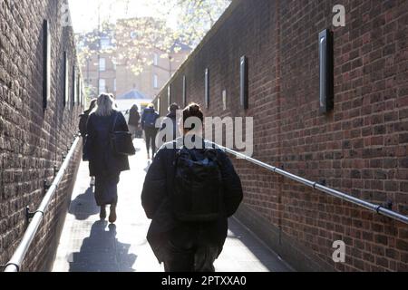 London, UK, 25 April 2023: At Pimlico tube station people walk up the ramp to exit the station on their way to work. Sunshine beams down on them and spring leaves on a tree can be seen in the distance. Anna Watson/Alamy Stock Photo