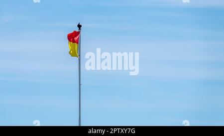 A red and yellow flag allowing swimming on the beach. flag on a sky background. Stock Photo