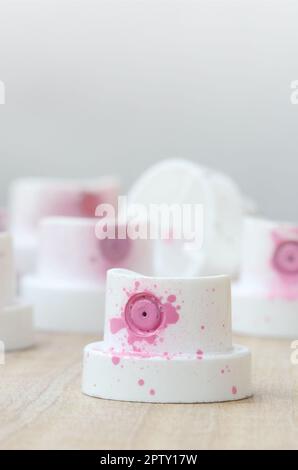 Several plastic nozzles from a paint sprayer that lie on a wooden surface against a gray wall background. The caps are smeared in pink paint. The conc Stock Photo