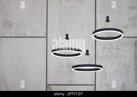 Unusual light sources hang on the background of a marble wall. Lamps in the form of a luminous ring Stock Photo