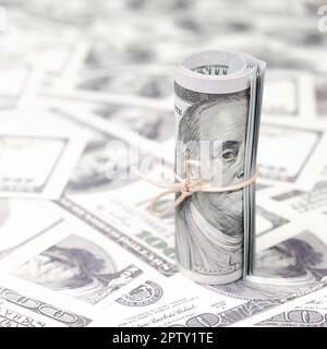 US dollars rolled up and tightened with band lies on a lot of american banknotes with blurred background. Big amount of money Stock Photo