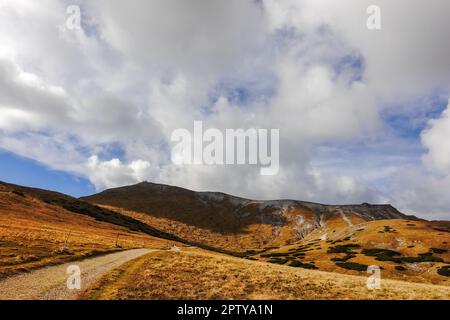 long dirt road through a hilly landscape at the top from a mountain in austria Stock Photo