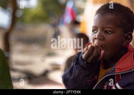An IDP  boy child eats rice out of a communal bowl with his family in Segou Region, Mali, West Africa. 2022 Mali drought and hunger crisis. Stock Photo