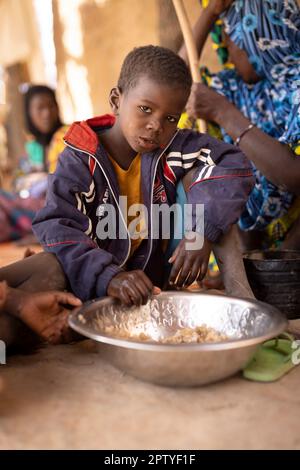 An IDP boy child eats rice out of a communal bowl with his family in Segou Region, Mali, West Africa. 2022 Mali drought and hunger crisis. Stock Photo