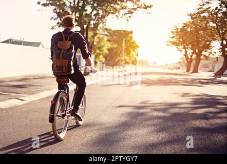 Taking a ride on the brighter side of life. Rearview shot of a young man riding a bicycle outdoors Stock Photo