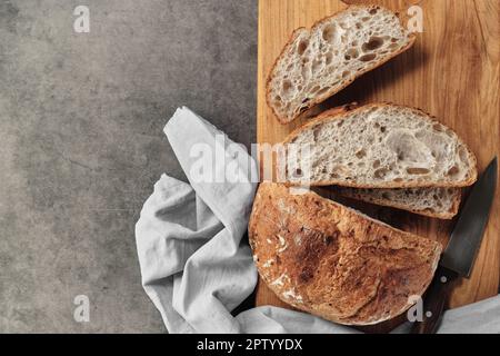 Sliced loaf of artisan sourdough bread on a cutting board on a gray concrete table. Top view with copy space. Stock Photo
