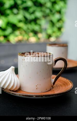 Cup of Turkish black frothy coffee on a black stone table with branches of wild ivy in the background, bizet next to the cup. Vertical frame, selectiv Stock Photo