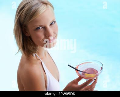 It doesnt get any better than this. a young woman drinking a cocktail by a swimming pool Stock Photo